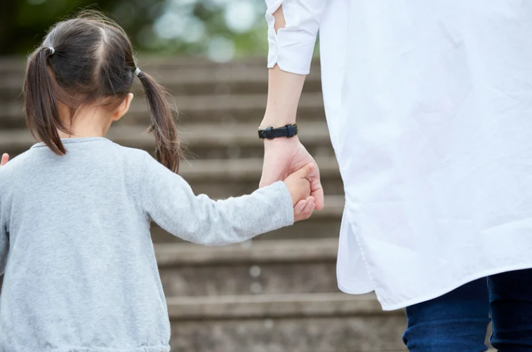 Parent holding a young child's hand on stone steps
